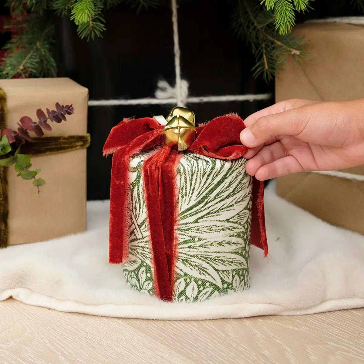 A wrapped candle under a Christmas tree, part of a tutorial on how to wrap a candle or cylinder.